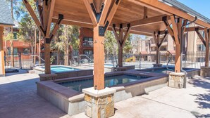 A covered outdoor pool area with multiple hot tubs, stone steps, and a wooden pergola structure.