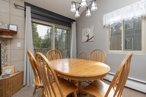 Un comedor con una mesa redonda de madera y seis sillas, una chimenea con detalles de piedra y un ventanal con cortinas.