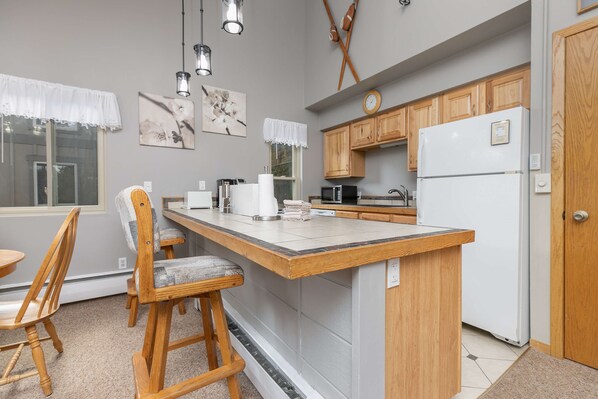 A kitchen with wooden cabinets, a white refrigerator, a bar stool, and a window with a view.