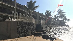 Ein Strandhotel mit einer Steinmauer, einer Treppe zum Strand und Palmen.