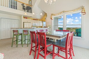 Una cocina amplia con comedor, que cuenta con una isla grande, gabinetes blancos y vistas al exterior.