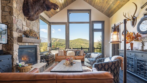 Un salon chaleureux avec une cheminée en pierre, des meubles en cuir et une grande fenêtre donnant sur un paysage montagneux.