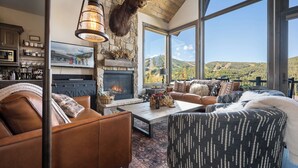 Un salon chaleureux avec une cheminée en pierre, des canapés en cuir et une grande fenêtre donnant sur une vue imprenable sur les montagnes.