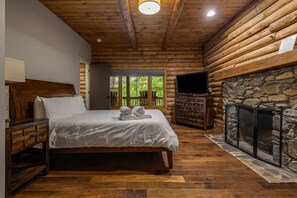 A log cabin bedroom with a bed, a television, and a stone fireplace.