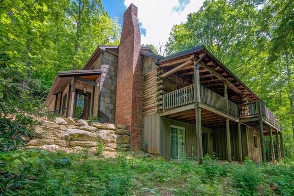 A rustic cabin with a stone foundation, wooden walls, and a balcony.