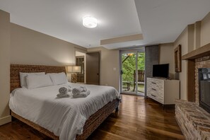 A bedroom with a large bed, a television, a fireplace, and a sliding glass door leading to an outdoor area.