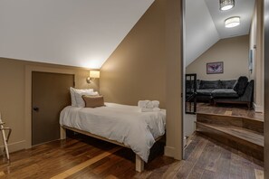A bedroom with a bed, a nightstand, a lamp, a door, and a staircase leading to a living area with a sofa.