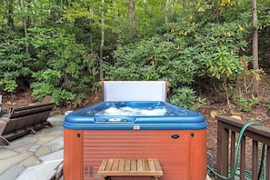 Un bain à remous installé à l’extérieur, avec une terrasse en bois et une végétation luxuriante en arrière-plan.