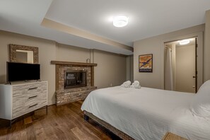 Un dormitorio con chimenea de ladrillo, un televisor de pantalla plana sobre una cómoda, una cama con ropa blanca y una puerta con toallero.