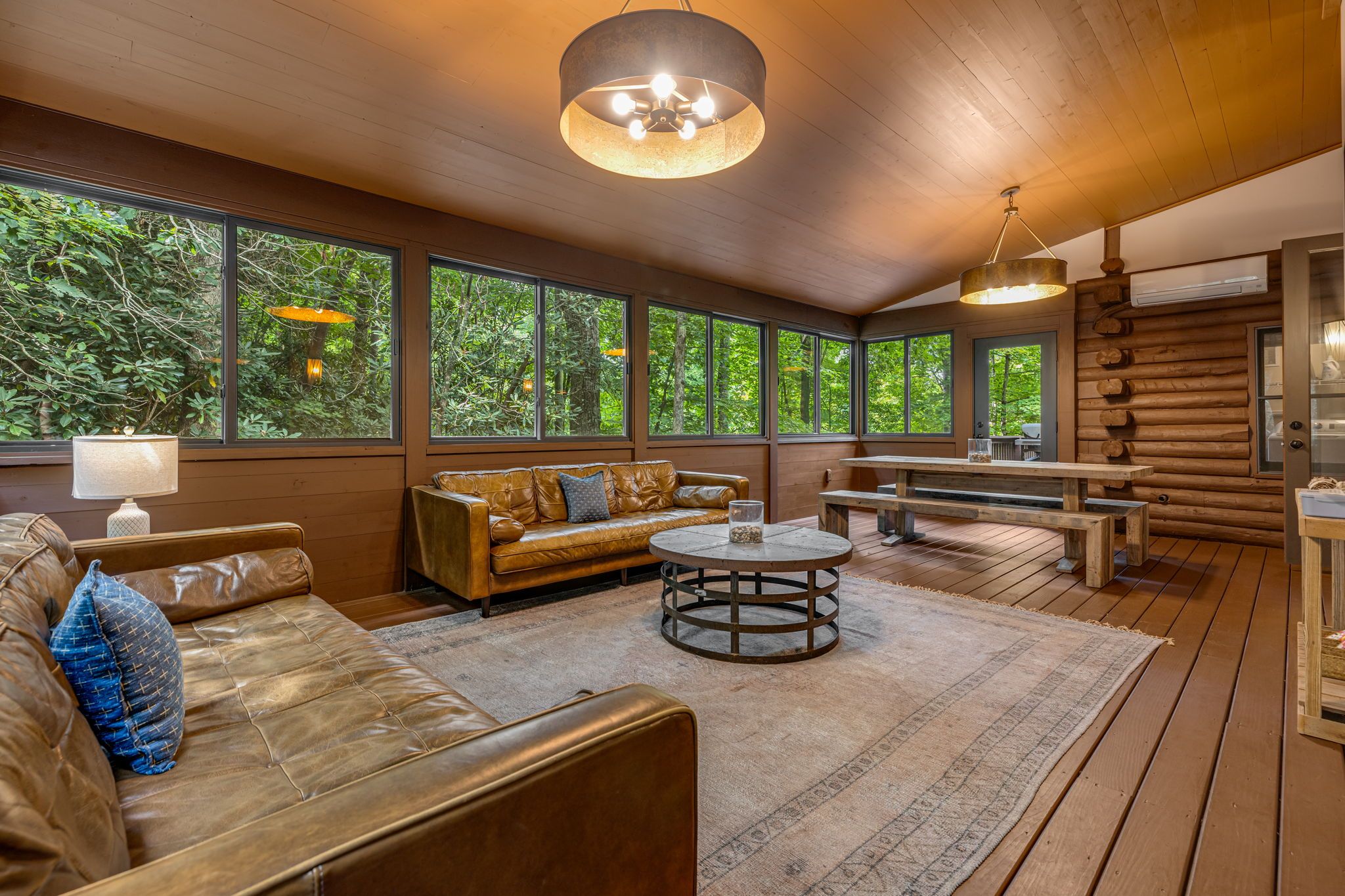 Un intérieur en bois avec un canapé en cuir, une table ronde et de grandes fenêtres donnant sur un espace verdoyant.