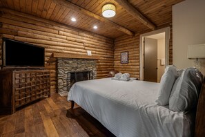 Una habitación tipo cabaña de madera con una cama, un televisor, una chimenea y una puerta.