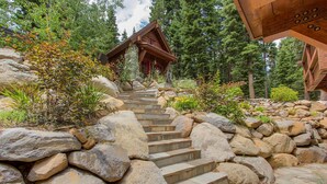 A wooden cabin with a stone staircase leading to a red door, surrounded by rocks and trees.