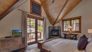 A bedroom with a large bed, a fireplace, a television, and a stone wall.