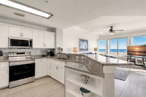A modern kitchen with white cabinetry, stainless steel appliances, and a view of the beach through large windows. - 3204 SeaCrest - Direct Oceanfront -March/April Heated Pool (Hilton Head Island)