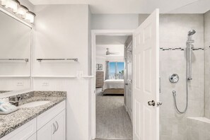 A modern bathroom with a shower, a vanity with a mirror, and a view to a bedroom. - 3204 SeaCrest - Direct Oceanfront -March/April Heated Pool (Hilton Head Island)