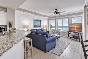 A modern living room with a large window, a sofa, a coffee table, and a TV. - 3204 SeaCrest - Direct Oceanfront -March/April Heated Pool (Hilton Head Island)