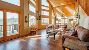 A spacious living room with large windows, wooden flooring, and a high ceiling. - Mountain Chalet w/ Hot Tub, Views & Game Room (McHenry)