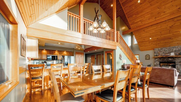 A spacious dining area with a high wooden ceiling and a central chandelier. A staircase leads to an upper level. - Mountain Chalet w/ Hot Tub, Views & Game Room (McHenry)