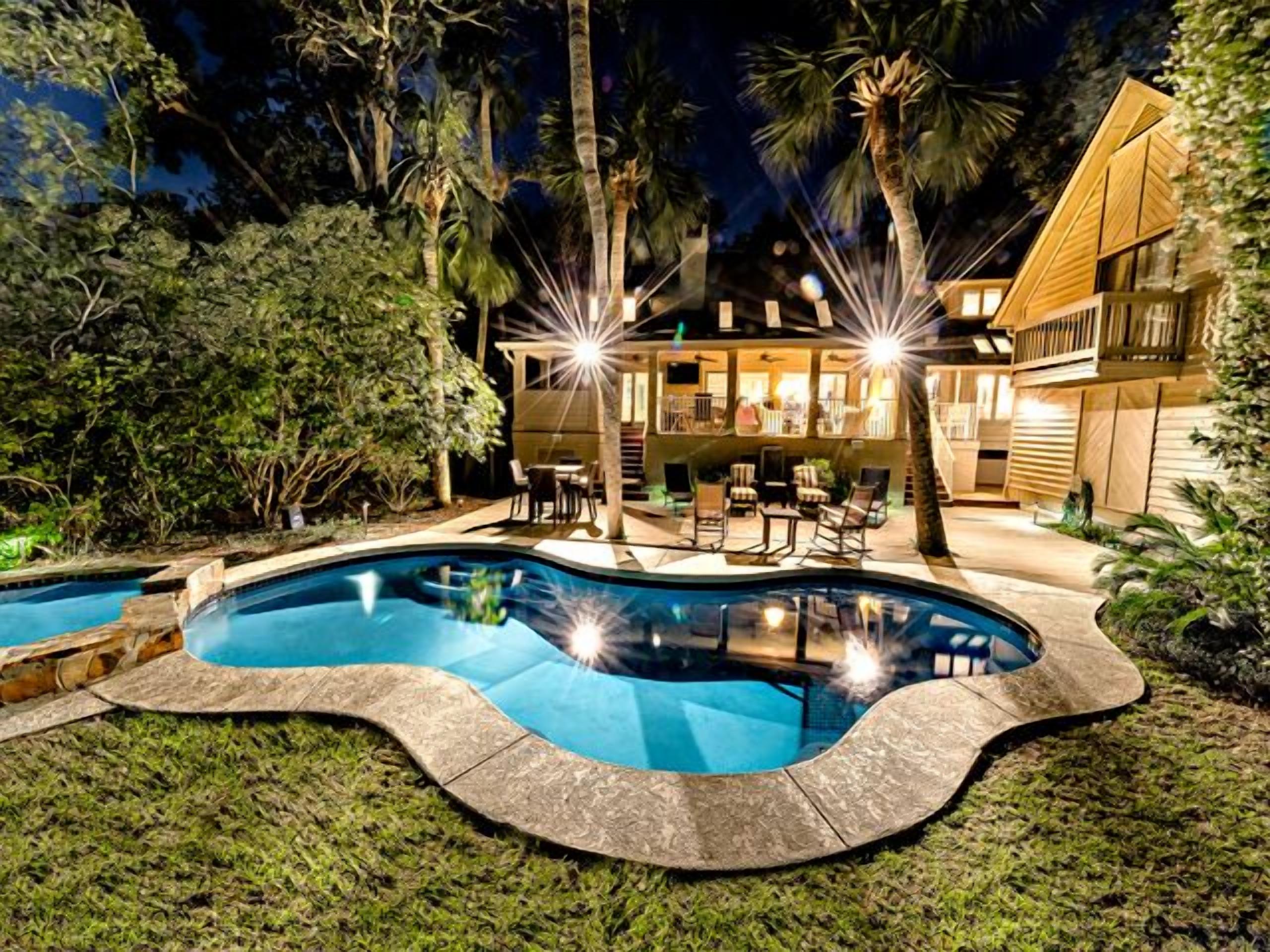 A swimming pool with a curved edge, surrounded by a well-maintained lawn and tropical plants.