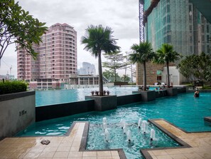 A swimming pool with a fountain, surrounded by palm trees and modern buildings. - Wallace P Staycation (Kuala Lumpur)