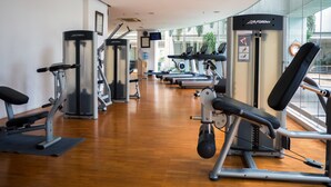 A gym with cardio machines, weight training equipment, and a wooden floor.
