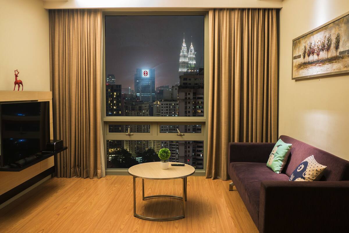 A modern living room with a large window, a round table, a sofa, and a TV.
