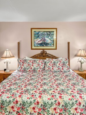Una cama con una colcha estampada con motivos florales, un cuadro enmarcado de cisnes y dos lámparas de noche.