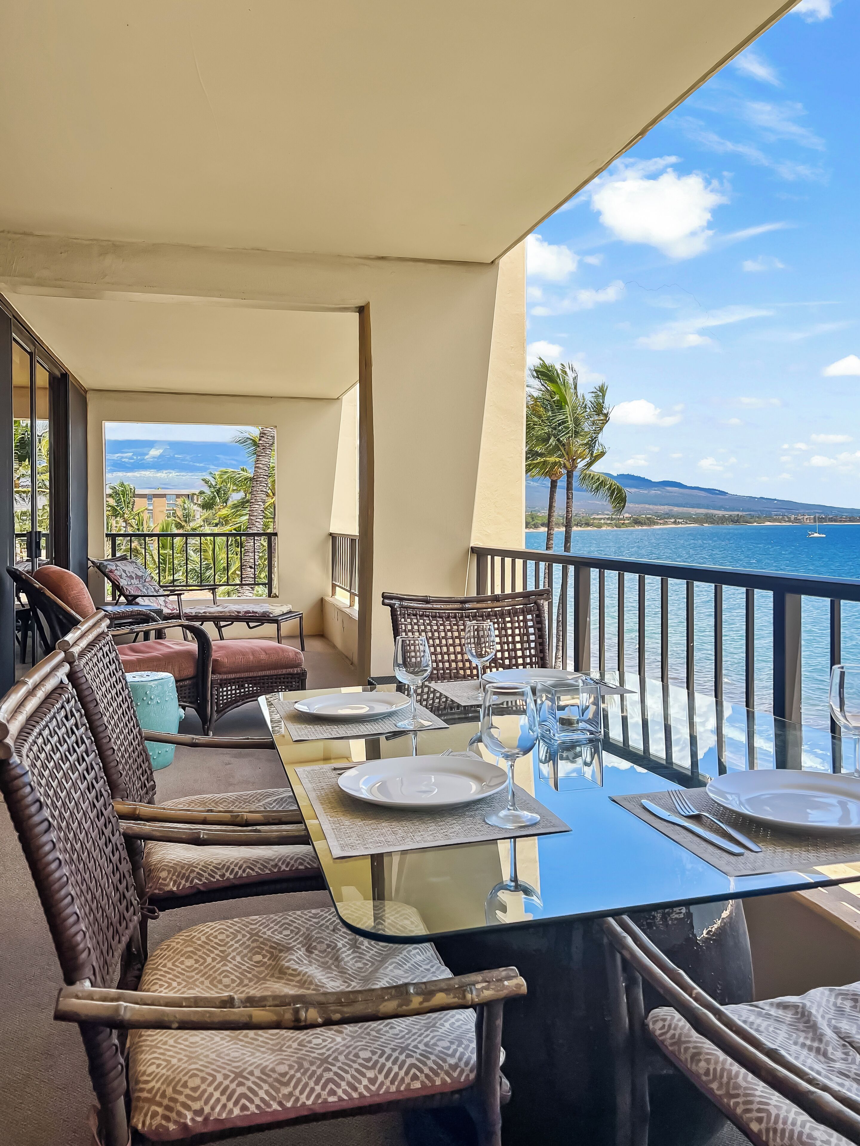 A dining area with a view of the ocean, furnished with wicker chairs and a glass table.