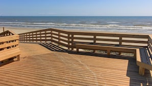 A wooden boardwalk leading to a beach with a wooden railing and benches.
