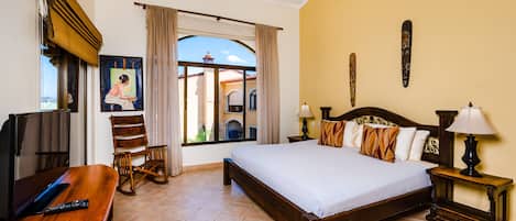 Habitación de hotel con una cama grande, un escritorio con una computadora portátil, una silla, un ventilador de techo y vistas al exterior.