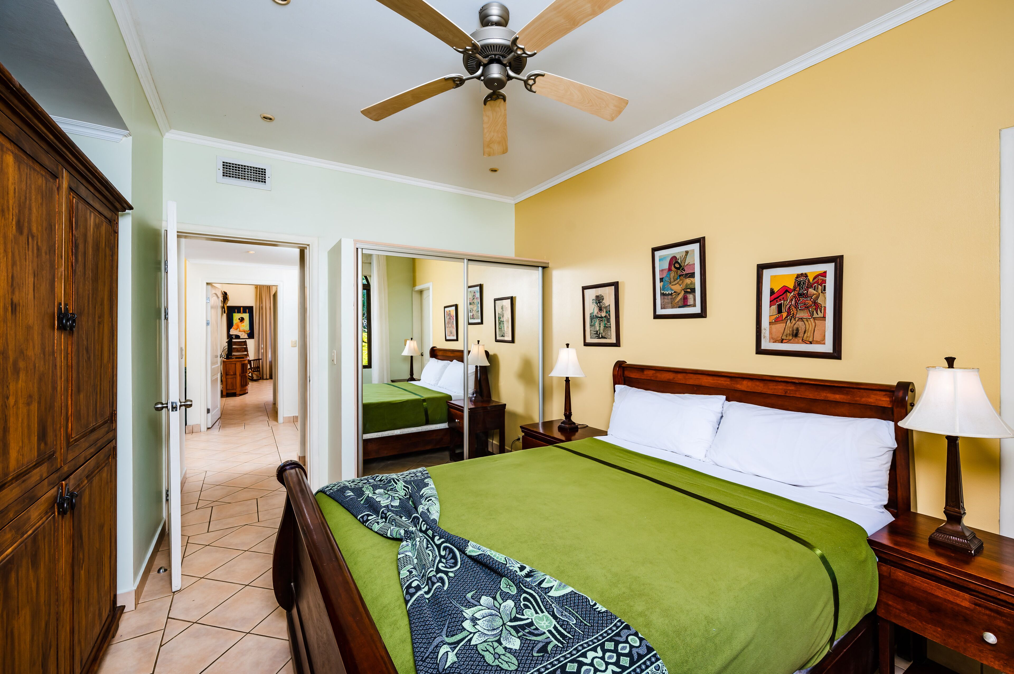 A hotel room with a bed, a nightstand, a ceiling fan, a wardrobe, and a mirror.