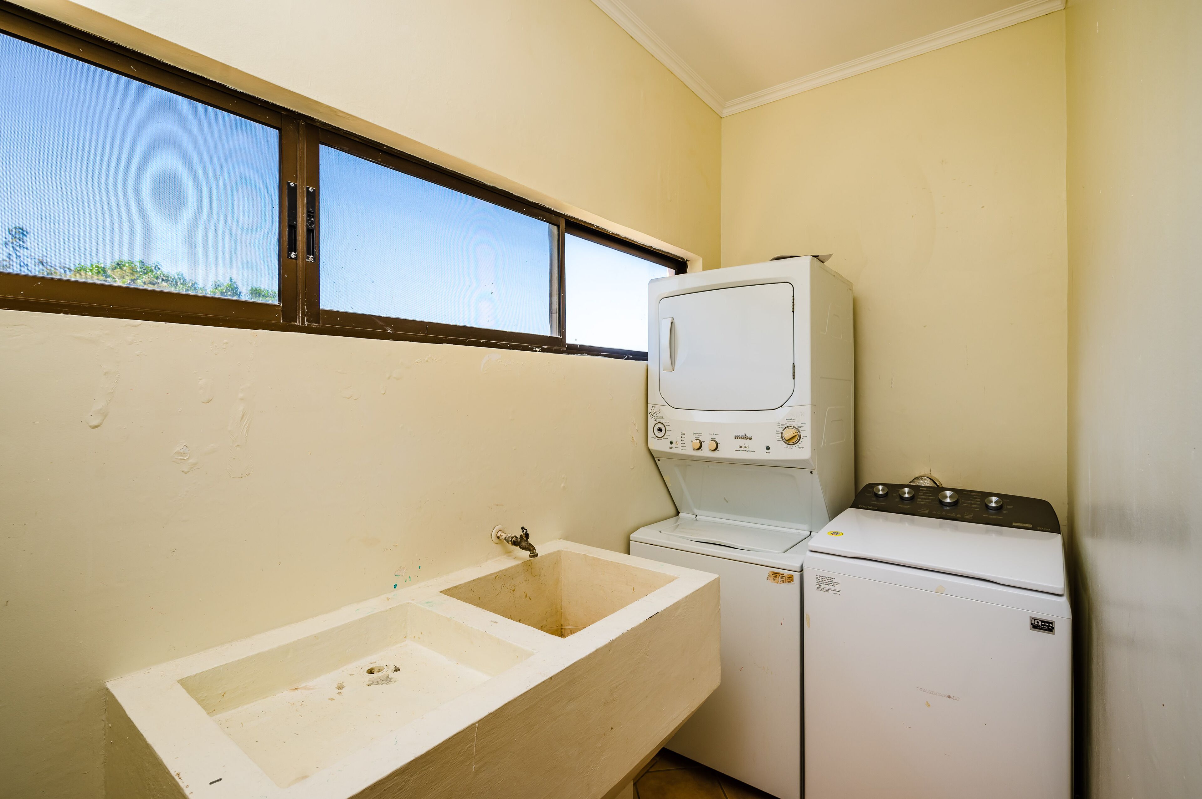 A laundry room with a washing machine, a sink, and a window.