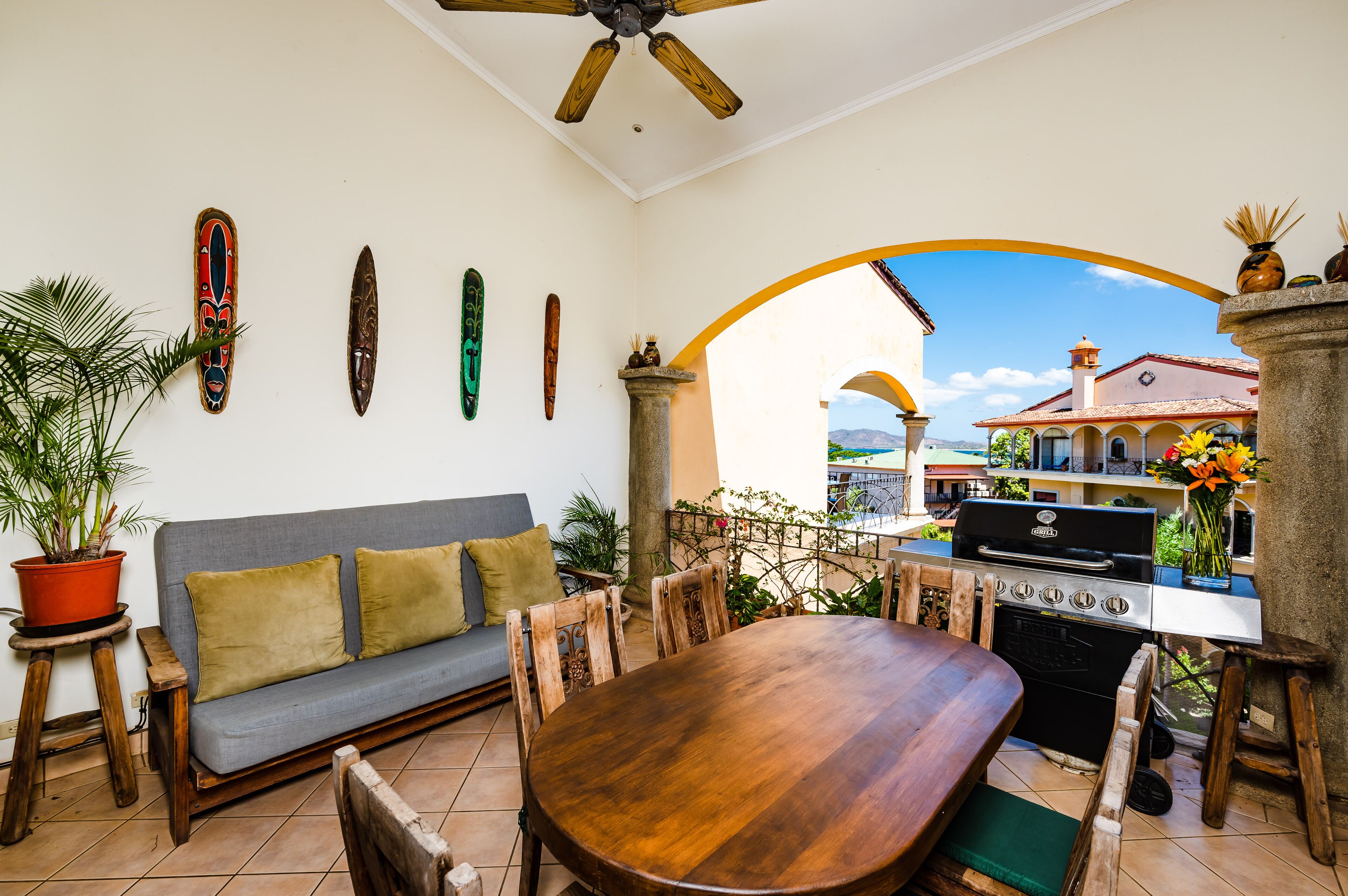 Eine Terrasse im Freien mit Holztisch und -stühlen, einem grauen Sofa und einem Grill.