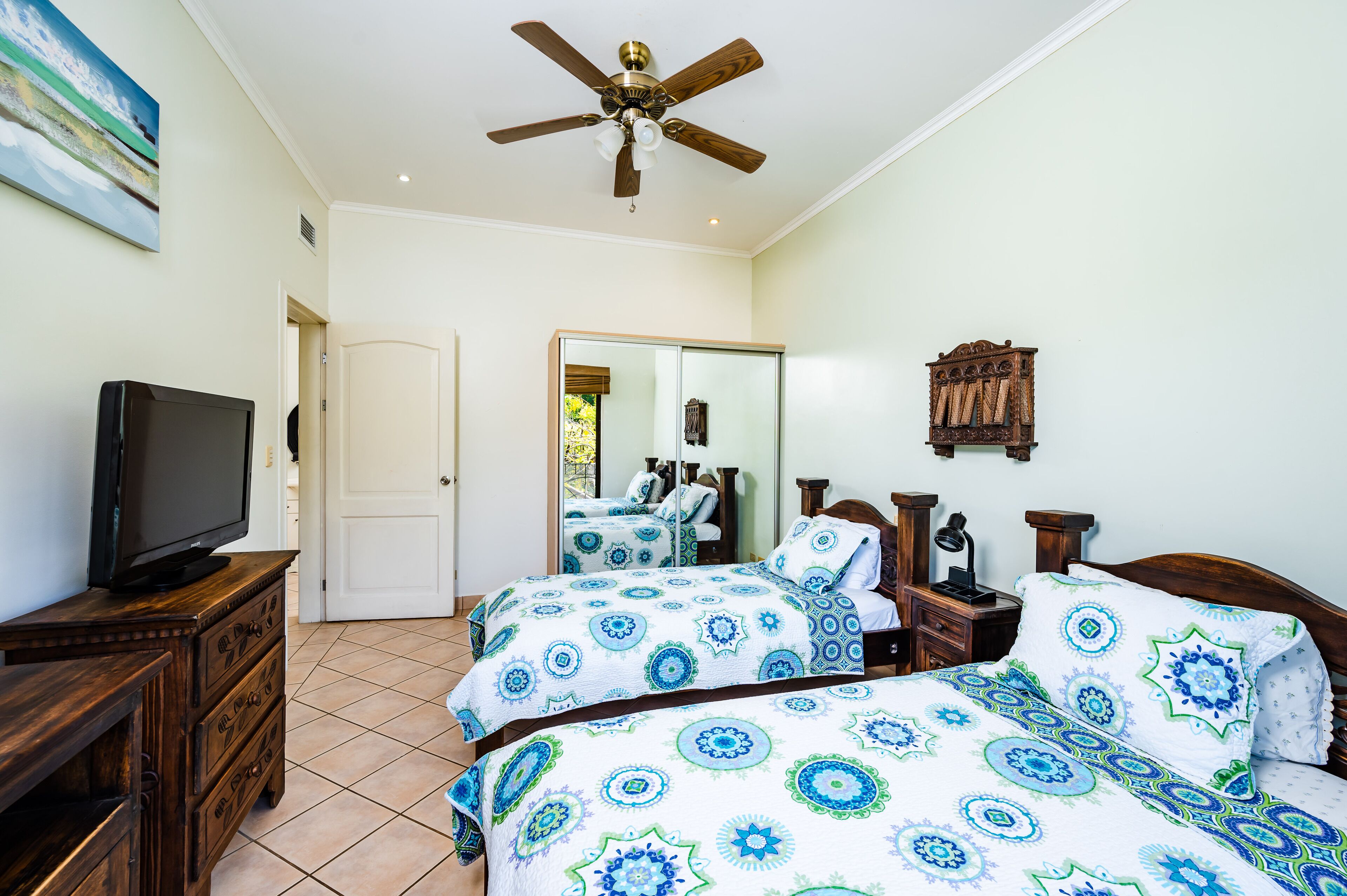 A bedroom with two beds, a ceiling fan, a television on a wooden dresser, and a mirror on the wall.