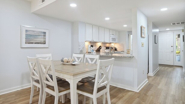 Une cuisine moderne avec des meubles blancs, un îlot central et un coin repas comprenant une table en bois et des chaises blanches.