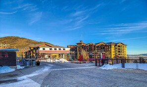 Hotel con telesilla, montañas al fondo y cielo despejado.