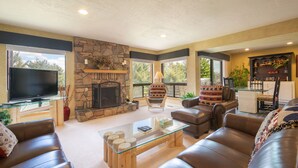A living room with a stone fireplace, leather sofas, a glass coffee table, and a television. - Park West Town Home 3920: 5 Bedroom 3.5 Bath (Park City)