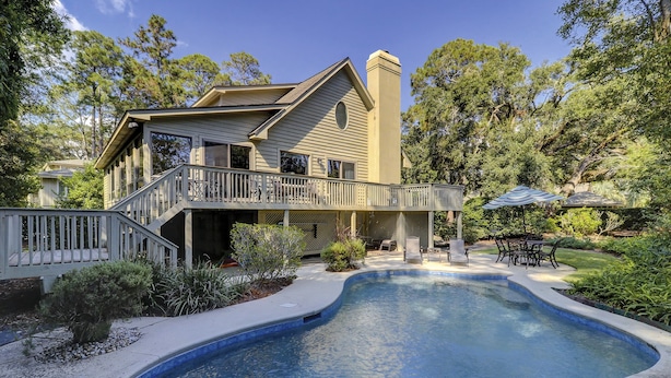Une maison à deux étages dotée d’une piscine, d’un patio couvert et d’une terrasse aménagée avec du mobilier d’extérieur.