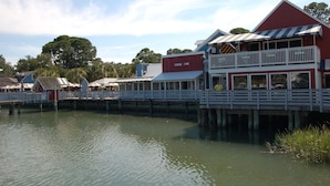 Un bâtiment situé au bord de l’eau, avec une enseigne indiquant qu’il s’agit d’une épicerie, une terrasse couverte et une jetée qui s’avance dans l’eau.