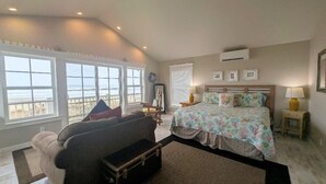 Una camera da letto con un letto grande, un divano, una finestra vista spiaggia e un condizionatore.