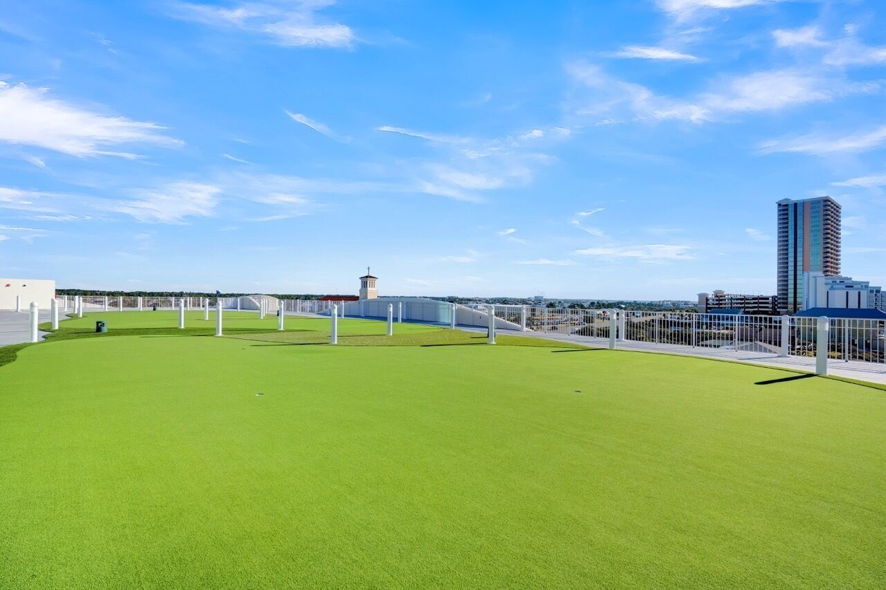 Eine Dachterrasse mit grünem Kunstgrün, weißen Geländern und einer Stadtansicht im Hintergrund.