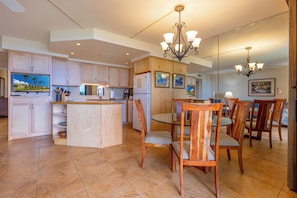 A spacious kitchen with wooden cabinets, a central island, and a dining area with chairs and a table. - Kihei Beach Resort #107: Your Tropical Paradise (Kihei)