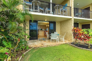 A two-story building with a balcony, a patio with outdoor furniture, and a garden area with tropical plants. - Kihei Beach Resort #107: Your Tropical Paradise (Kihei)