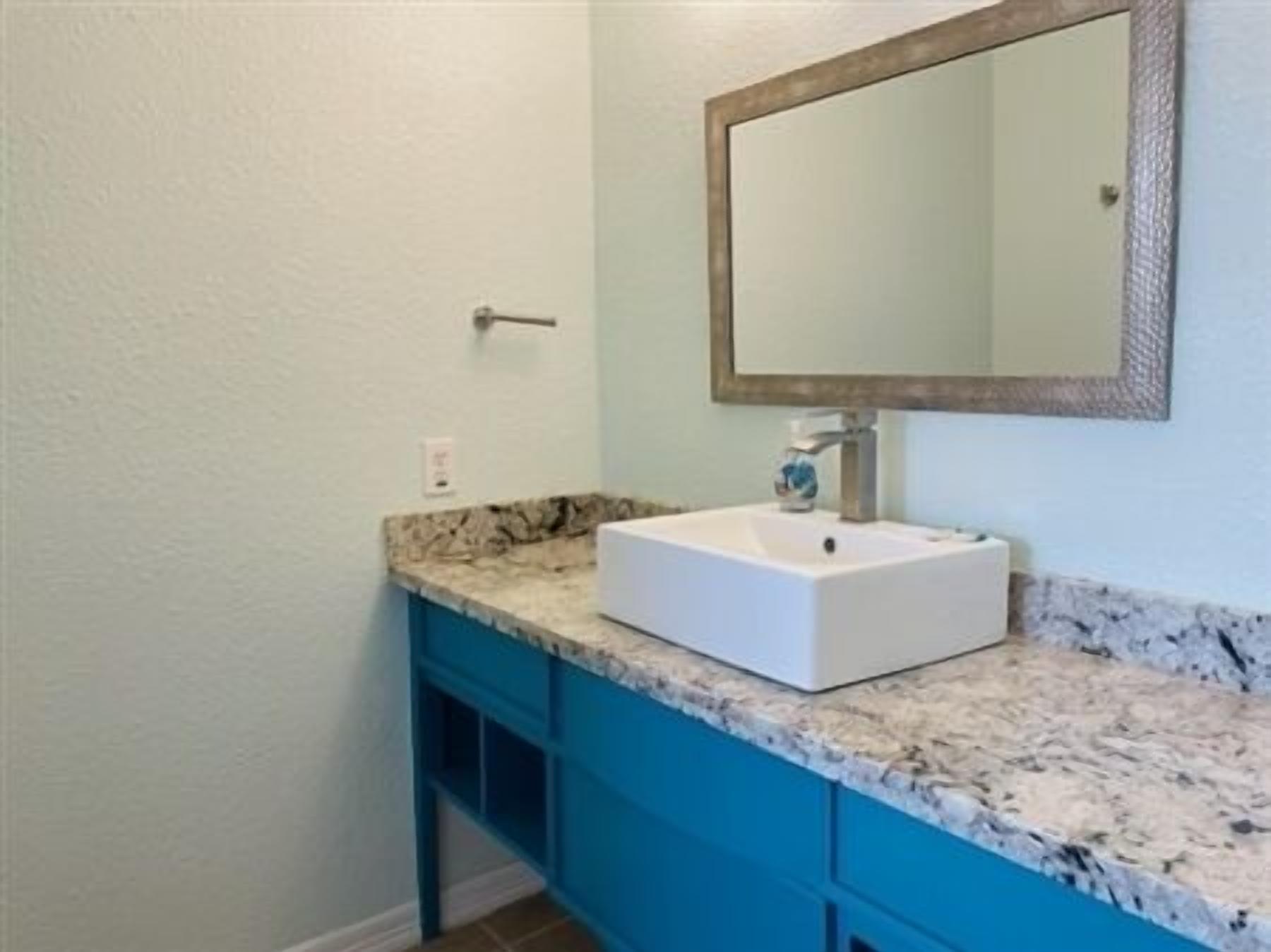 Casa de banho com lavatório branco, armários azuis e bancada de mármore.