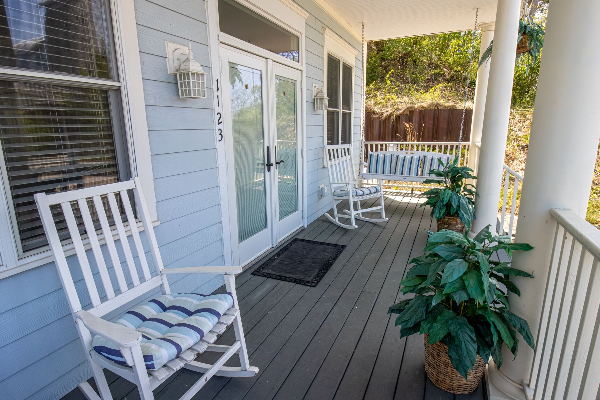 A porch with white rocking chairs and a door with glass panels.