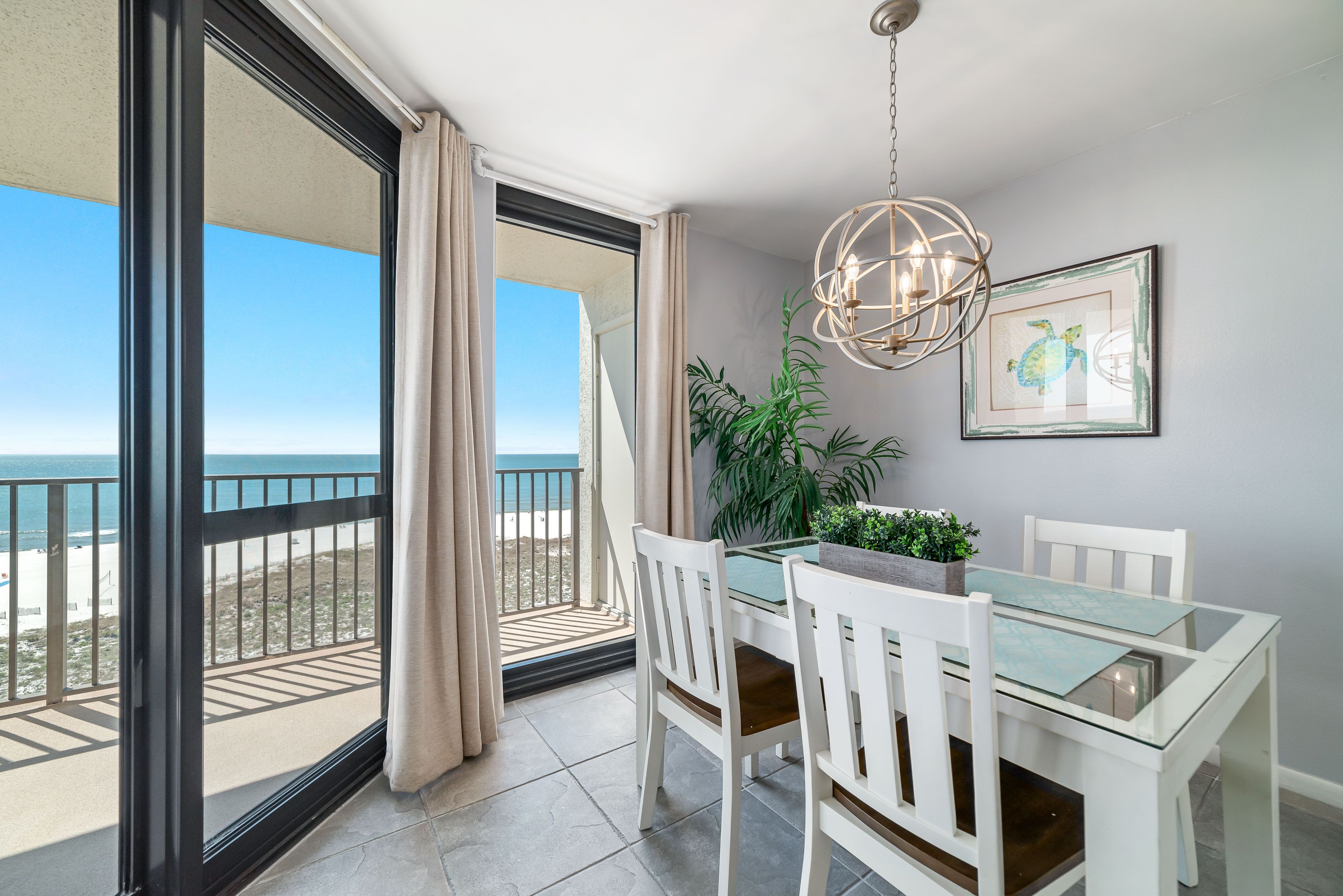 A balcony with a glass table and chairs, a hanging light fixture, and a framed picture on the wall.