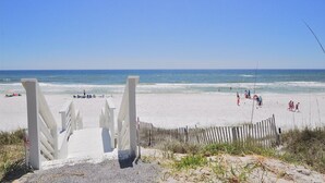 Une plage avec un escalier en bois menant à la grève, une clôture en bois et des personnes sur la plage.