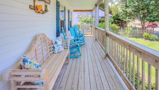A wooden porch with blue chairs and a bench, a sign reading "La Sirenita," and a view of a garden and street.