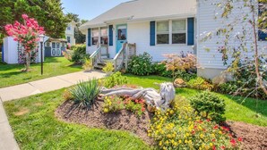 A single-story house with a front porch, a small garden with various plants and flowers, and a pathway leading to the entrance.