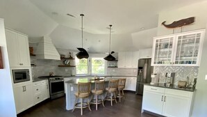 A modern kitchen with white cabinets, a central island with chairs, and a large refrigerator.
